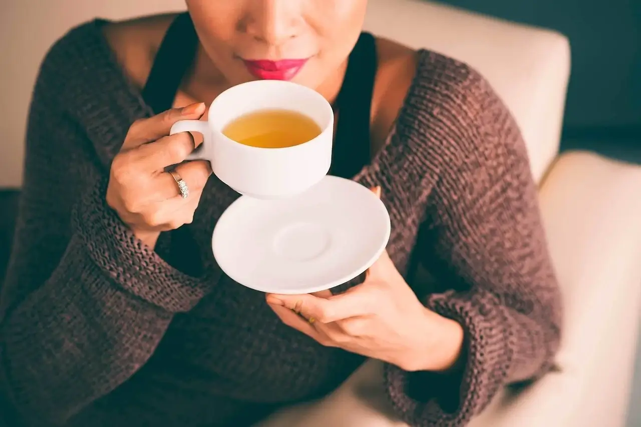A person carefully tasting and evaluating different types of tea in small cups.