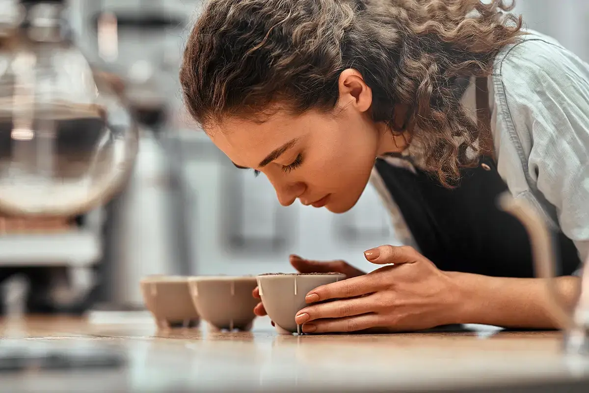 A quality control expert cupping coffee, smelling the aroma from a bowl.