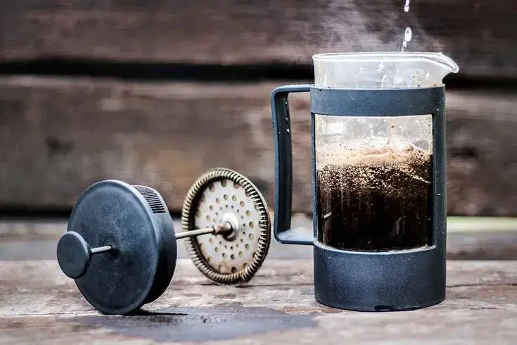 A classic French press filled with coarse coffee grounds.